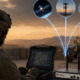 How ComBOX Keeps US Army Forces Connected Across the Middle East soldier using rugged laptop with communication device and satellite links in desert environment